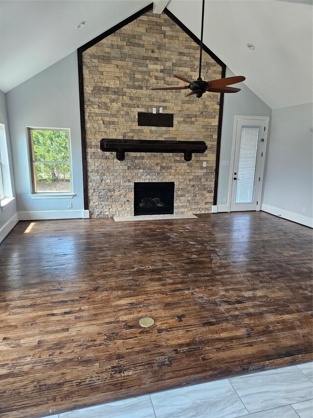 unfurnished living room featuring a stone fireplace, hardwood / wood-style floors, high vaulted ceiling, ceiling fan, and beam ceiling