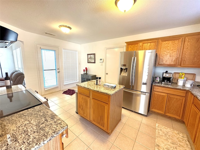 kitchen with a center island, stainless steel fridge with ice dispenser, light tile patterned floors, and light stone countertops