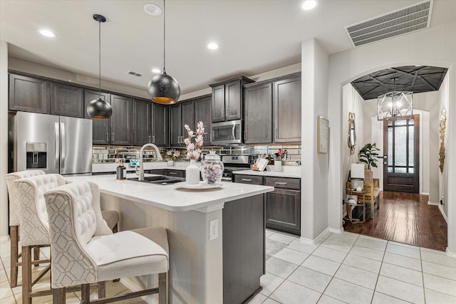 kitchen with sink, stainless steel appliances, an island with sink, pendant lighting, and dark brown cabinets