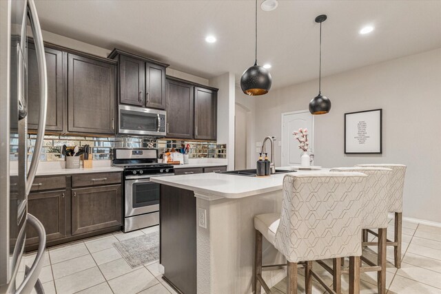 kitchen with tasteful backsplash, a breakfast bar, stainless steel appliances, pendant lighting, and an island with sink