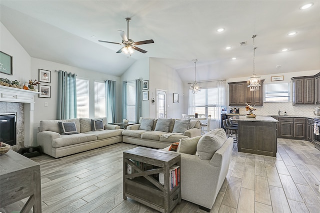 living room featuring a fireplace, light hardwood / wood-style flooring, high vaulted ceiling, and ceiling fan with notable chandelier