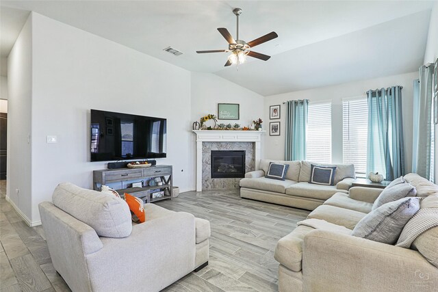 living room with lofted ceiling, visible vents, a high end fireplace, a ceiling fan, and light wood finished floors