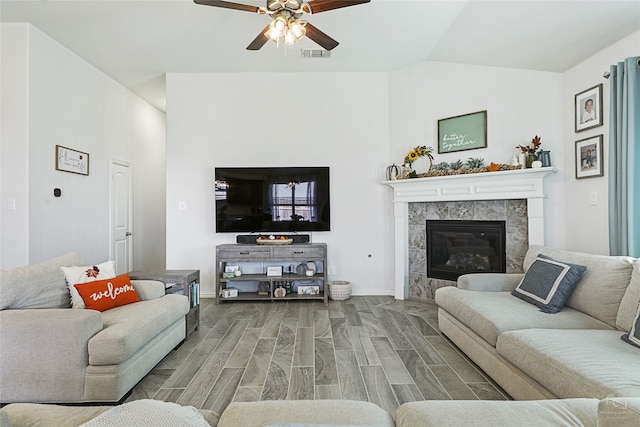 living area featuring lofted ceiling, visible vents, a tiled fireplace, a ceiling fan, and wood finished floors