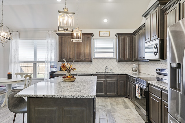 kitchen featuring appliances with stainless steel finishes, decorative light fixtures, a sink, and a kitchen island