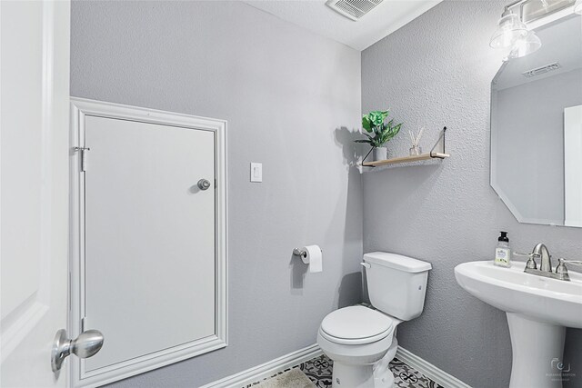 half bath with toilet, baseboards, visible vents, and a sink