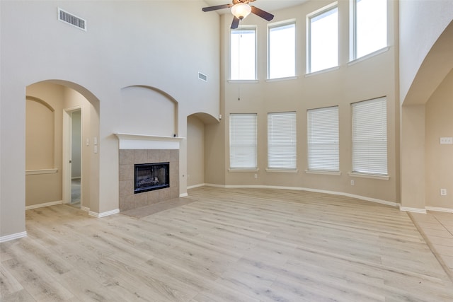 unfurnished living room with a high ceiling, light wood-type flooring, ceiling fan, and a fireplace