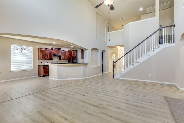 unfurnished living room featuring light hardwood / wood-style flooring, ceiling fan with notable chandelier, and a towering ceiling