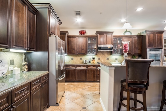 kitchen with dark brown cabinetry, light stone countertops, stainless steel appliances, decorative light fixtures, and decorative backsplash