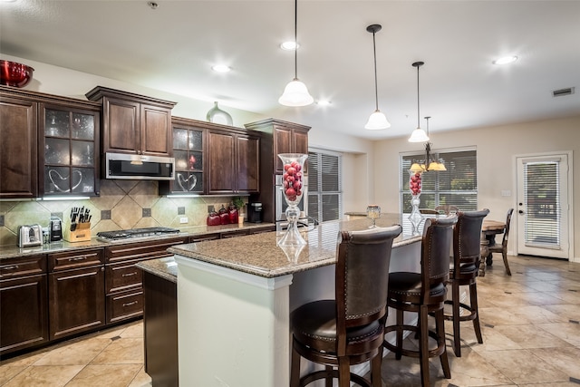 kitchen with light stone countertops, dark brown cabinetry, pendant lighting, a kitchen island, and stainless steel gas stovetop