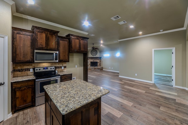 kitchen featuring stainless steel appliances, light stone counters, a kitchen island, a fireplace, and light hardwood / wood-style flooring