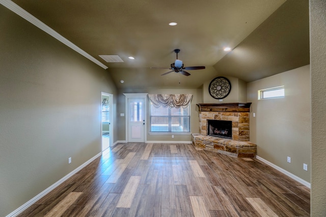 unfurnished living room with ornamental molding, a stone fireplace, vaulted ceiling, hardwood / wood-style flooring, and ceiling fan