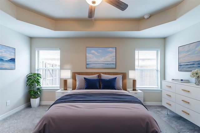 bedroom with a raised ceiling, light carpet, multiple windows, and ceiling fan