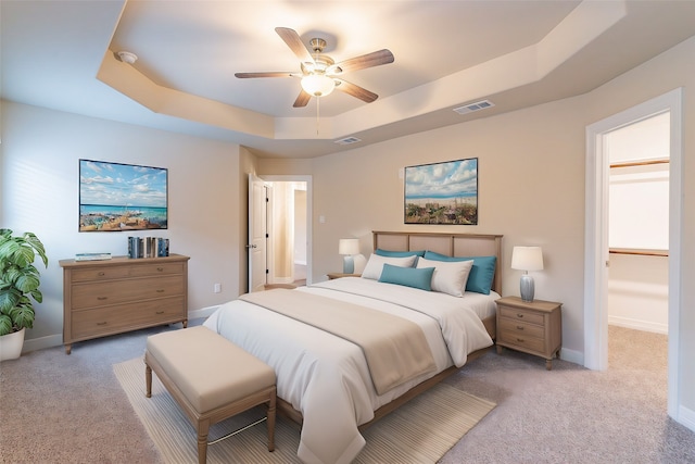 carpeted bedroom featuring a walk in closet, ceiling fan, and a tray ceiling