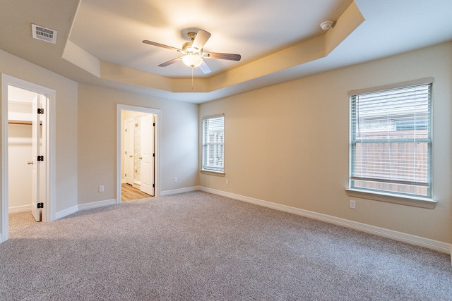 spare room with light colored carpet, ceiling fan, and a raised ceiling