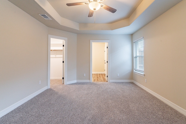 unfurnished bedroom with ceiling fan, light carpet, a spacious closet, and a tray ceiling