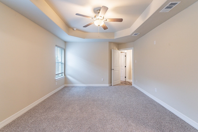 carpeted empty room with ceiling fan and a tray ceiling