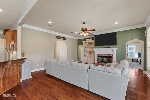 living room featuring dark hardwood / wood-style flooring, ceiling fan, ornamental molding, and a fireplace