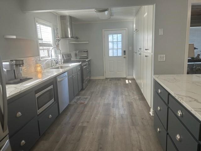 kitchen featuring appliances with stainless steel finishes, sink, white cabinets, light stone countertops, and wall chimney range hood