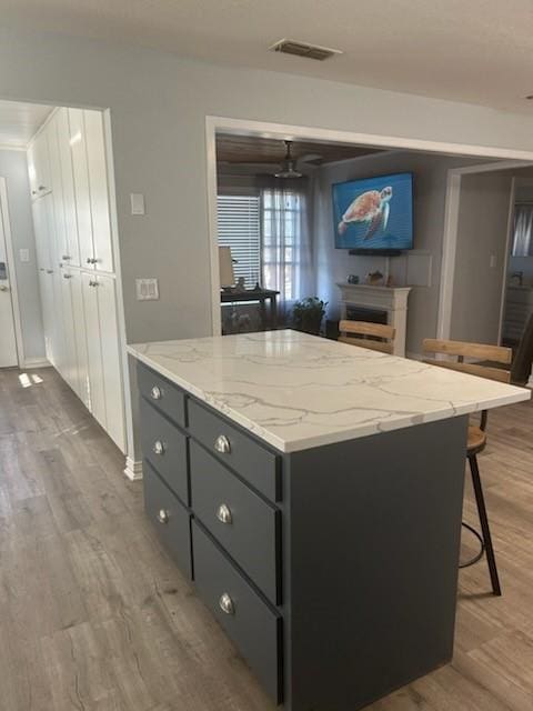 kitchen featuring a kitchen island, white cabinets, ceiling fan, light stone counters, and light wood-type flooring