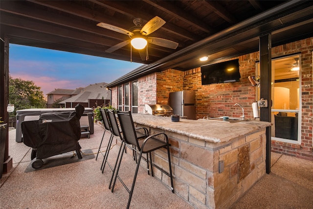 patio terrace at dusk featuring ceiling fan, an outdoor wet bar, exterior kitchen, and area for grilling