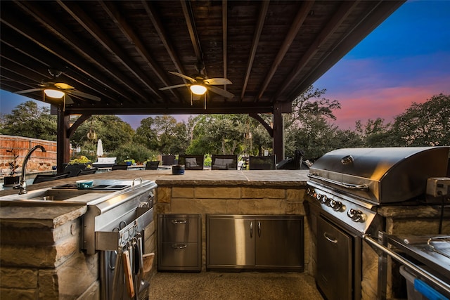 patio terrace at dusk featuring exterior kitchen, area for grilling, and ceiling fan