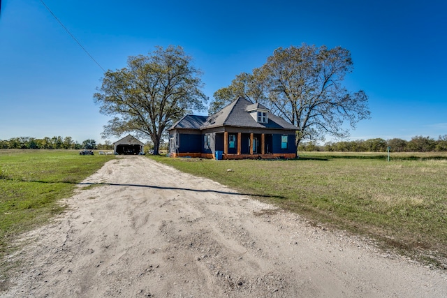 view of front of home featuring covered porch, a rural view, a front yard, and an outdoor structure