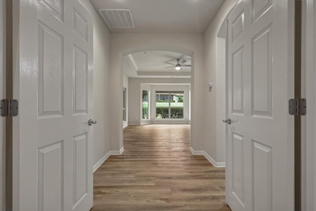 corridor with light hardwood / wood-style floors and a raised ceiling