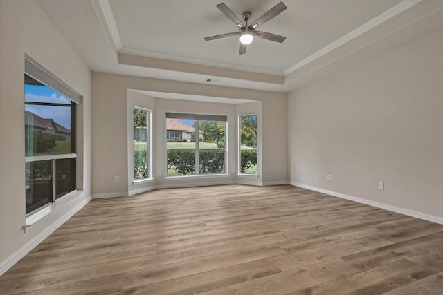 empty room with a tray ceiling, ceiling fan, ornamental molding, and light wood-type flooring