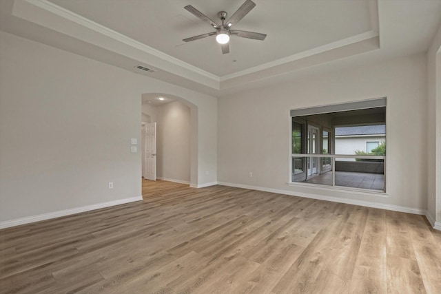 unfurnished room featuring ceiling fan, light wood-type flooring, ornamental molding, and a tray ceiling