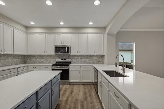 kitchen with light wood-type flooring, ornamental molding, stainless steel appliances, sink, and white cabinetry