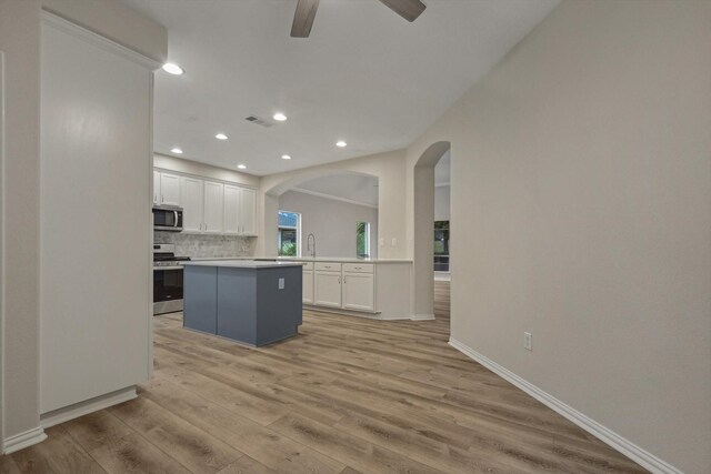 kitchen with a kitchen island, white cabinets, light wood-type flooring, and appliances with stainless steel finishes