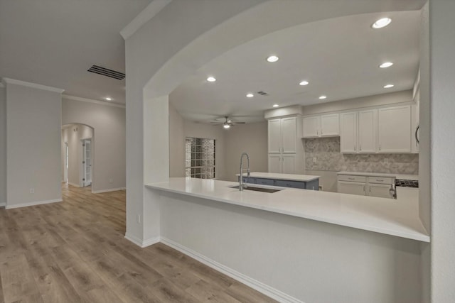 kitchen featuring white cabinetry, sink, light hardwood / wood-style flooring, kitchen peninsula, and decorative backsplash