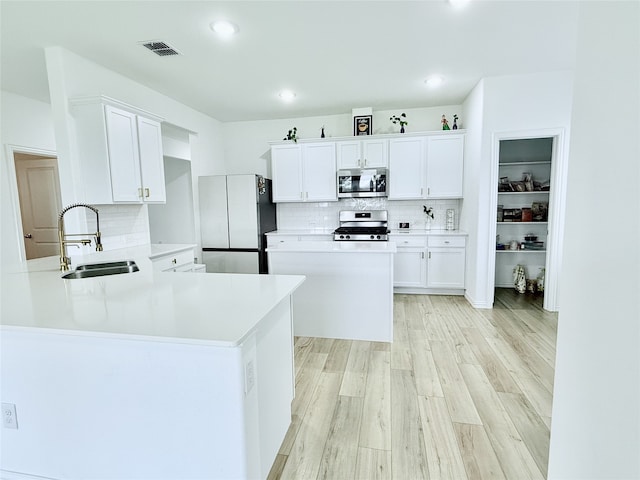 kitchen featuring light hardwood / wood-style flooring, white cabinets, sink, decorative backsplash, and stainless steel appliances