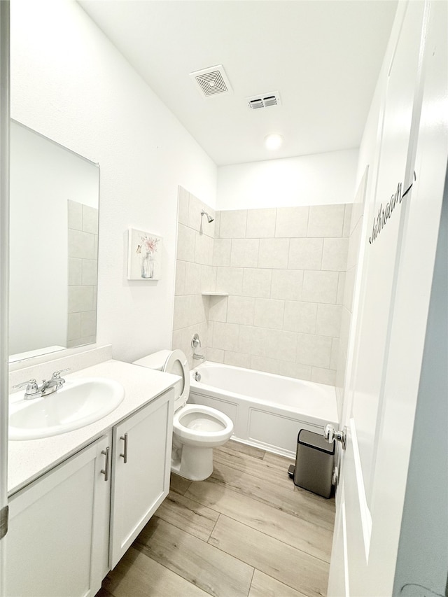 full bathroom with hardwood / wood-style floors, vanity, tiled shower / bath combo, and toilet