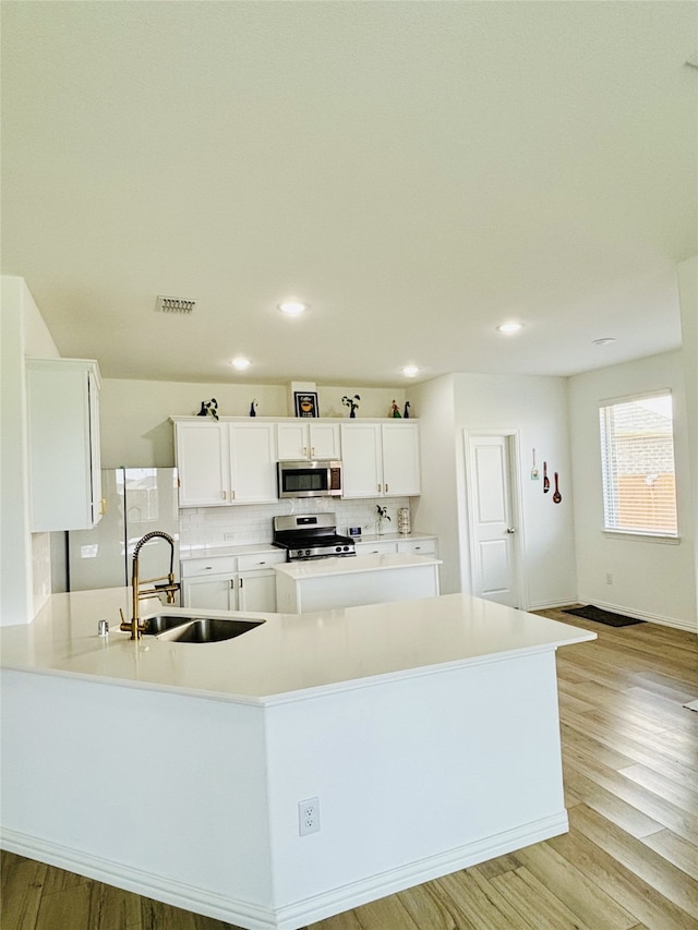 kitchen with white cabinets, light wood-type flooring, stainless steel appliances, and tasteful backsplash