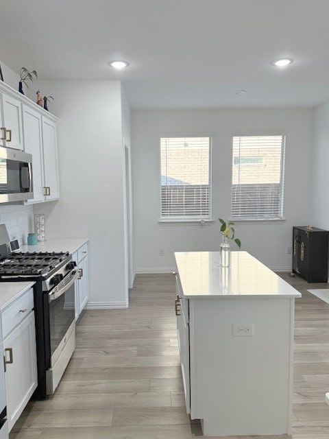 kitchen with appliances with stainless steel finishes, light wood-type flooring, tasteful backsplash, a kitchen island, and white cabinetry