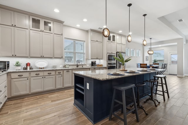 kitchen with light stone counters, stainless steel appliances, sink, a kitchen island, and hanging light fixtures