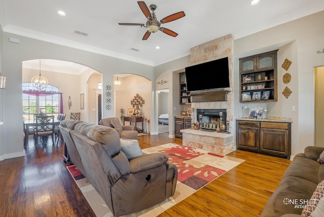 living room with a stone fireplace, wood-type flooring, ceiling fan with notable chandelier, and ornamental molding