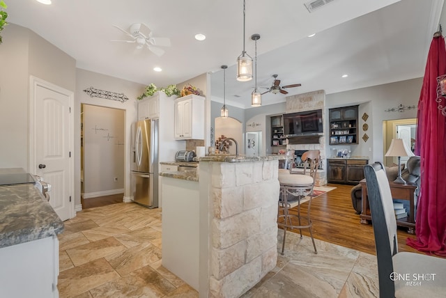 kitchen featuring white cabinets, a kitchen breakfast bar, hanging light fixtures, stainless steel fridge, and stone countertops