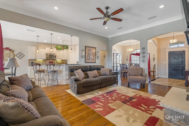 living room with ceiling fan with notable chandelier, light wood-type flooring, and ornamental molding