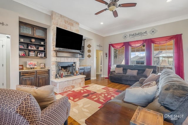 living room with ceiling fan, light wood-type flooring, a fireplace, and ornamental molding