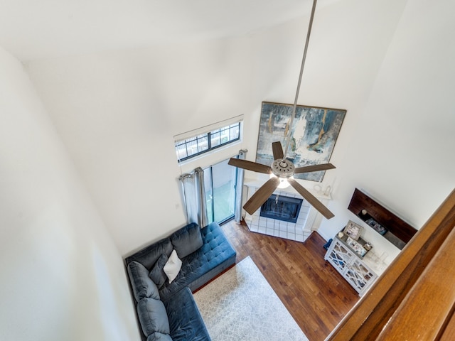 living room featuring a tile fireplace, wood-type flooring, a towering ceiling, and ceiling fan