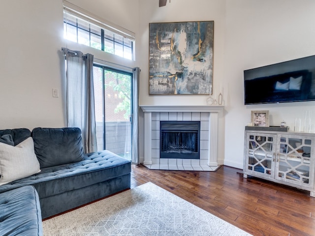 living room with wood-type flooring, a high ceiling, and a tiled fireplace