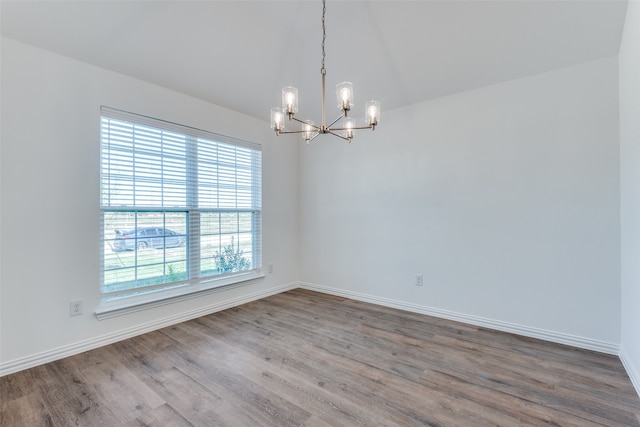 empty room featuring wood-type flooring, lofted ceiling, and an inviting chandelier