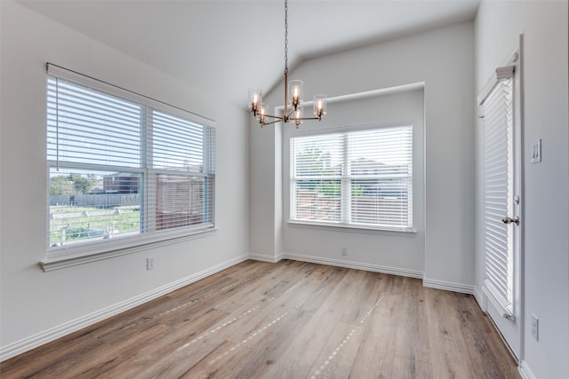 empty room with plenty of natural light, a chandelier, lofted ceiling, and light hardwood / wood-style flooring