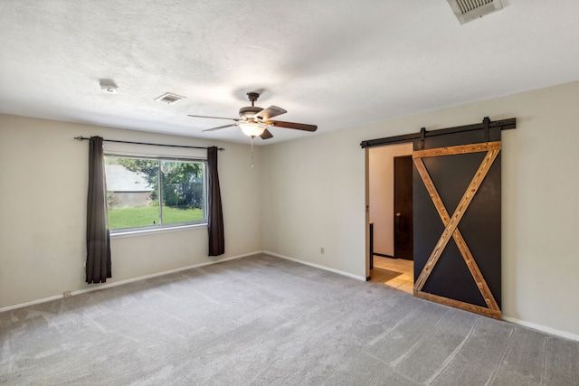 empty room featuring a barn door, light carpet, ceiling fan, and a textured ceiling