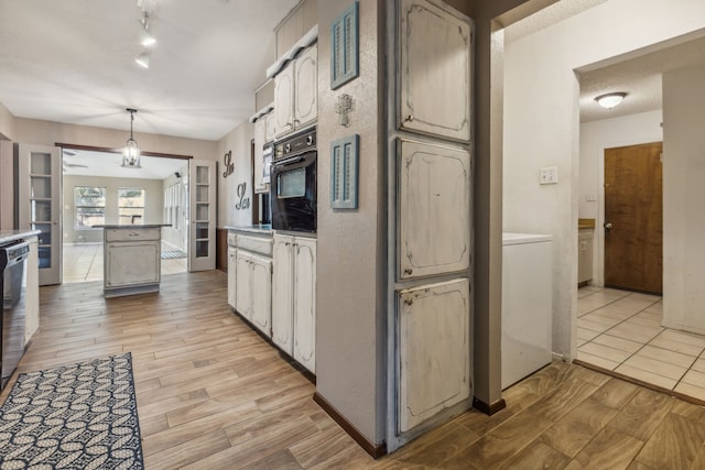 kitchen featuring white cabinetry, washer / clothes dryer, decorative light fixtures, black oven, and light wood-type flooring