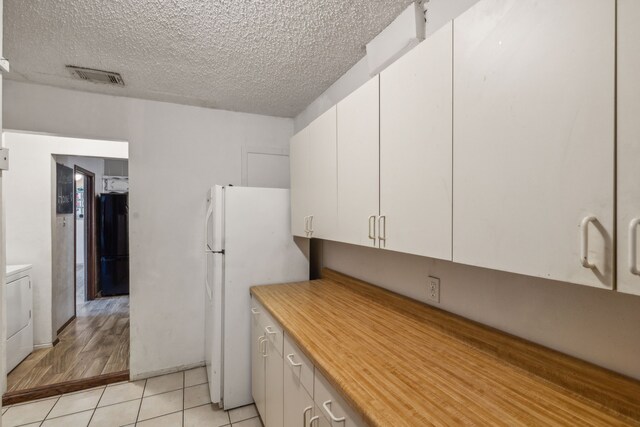 kitchen with white cabinetry, light hardwood / wood-style flooring, white refrigerator, a textured ceiling, and washer / dryer