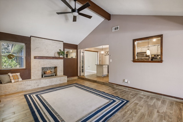 living room featuring ceiling fan with notable chandelier, hardwood / wood-style floors, vaulted ceiling with beams, and a brick fireplace