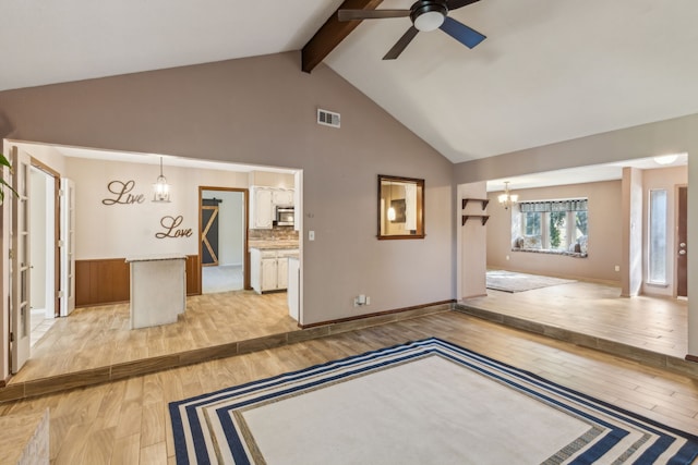 unfurnished living room featuring beamed ceiling, ceiling fan with notable chandelier, high vaulted ceiling, and light hardwood / wood-style flooring